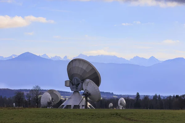 Parabolic antennas of the satellite communication system of the earth station near Raisting at the Ammersee in partly cloudy sky in front of the panorama of the Alps