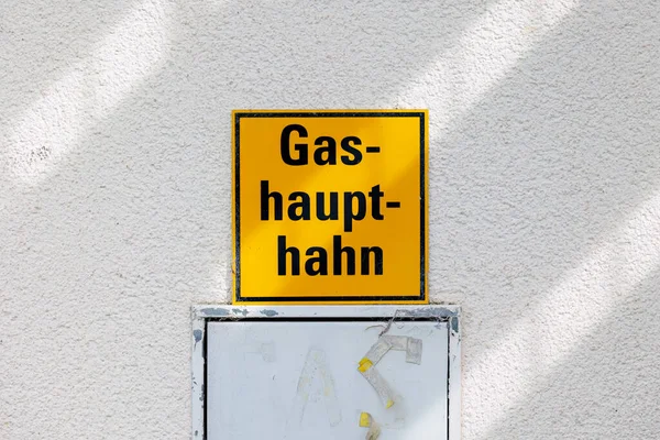 A yellow sign on a house wall with the German text Gas Main Shut-off Valve
