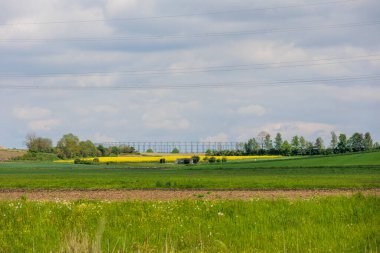 Augsburg yakınlarındaki Schmutter Vadisi 'nde yeşil çayırlar ve sarı çiçek açan tecavüz tarlaları üzerindeki BND saha ofisi Gablingen manzarası