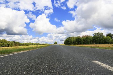 Yukarı Franconia 'daki kır yolu mavi gökyüzü ve kümülüs bulutları ile çayırlar ve ormanlar arasında.