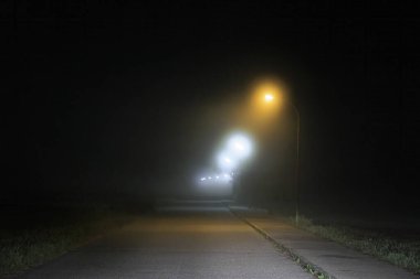 Gece ufka giden bir yol var. Sisin altındaki sokak lambalarının altında.