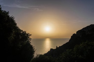 Güneş, Agios Spiridon yakınlarındaki Agios Spiridon adasında sahil siluetine karşı altın renginde batıyor.