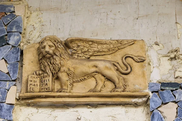 A stone relief of a winged lion with a book in its hand on a wall on the island of Corfu