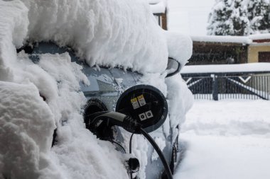 Derin karla kaplı elektrikli bir araba, 2 Aralık 2023 'te Almanya, Augsburg, Tip 2 şarj prizi ile şarj edilir.
