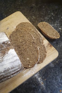 Dilimlenmiş taze, sıcak, siyah ev yapımı ekmek ahşap fırından buharla doğranmış bir tahtanın üzerinde.