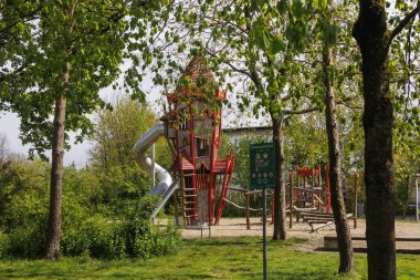 Parlak kırmızı oyun kulesi olan bir oyun alanı ve bulutlu bir günde Augsburg, Bavyera yakınlarındaki Konigsbrunn 'da kayıyor.