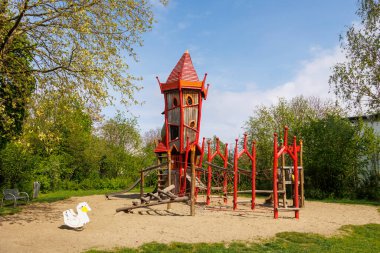 Parlak kırmızı oyun kulesi olan bir oyun alanı ve bulutlu bir günde Augsburg, Bavyera yakınlarındaki Konigsbrunn 'da kayıyor.