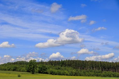 Kümülüs bulutları mavi gökyüzünde çayırlar ve ormanlar üzerinde