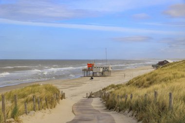 Hollanda 'da Petten aan Zee' de bulutlu gökyüzü olan fırtınalı bir günde cankurtaran kulübesi olan sahile giden patika.