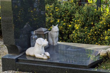 Beyaz kedi ve beyaz köpek figürlü siyah cilalı mermer bir mezar taşı.