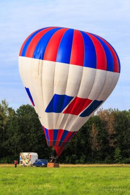 Kırmızı ve mavi renkli iki sıcak hava balonu kalkıştan önce ormanın kenarındaki bir çayırda sıcak havayla doldurulur.