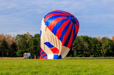 Kırmızı ve mavi renkli iki sıcak hava balonu kalkıştan önce ormanın kenarındaki bir çayırda sıcak havayla doldurulur.