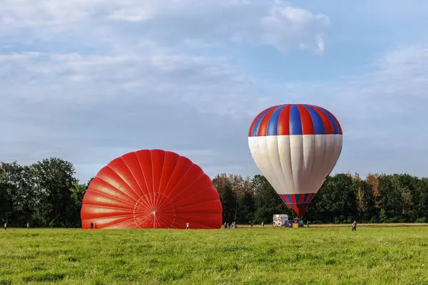 stock image Two hot air balloons in the colours red and blue are pre-filled with hot air on a meadow at the edge of the forest before the launch