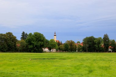 Augsburg yakınlarındaki Merching 'de bulutlu bir gökyüzünün altındaki çayır ve tarım binalarına bakın.