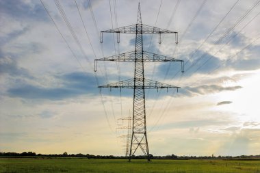 Bulutlu bir akşam gökyüzünün önündeki çayırda bir elektrik hattı.
