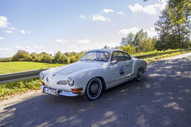 Fildişi renkli Karman Ghia 1500, Raisting am Ammersee 'de Fuggerstadt Classics, Almanya' da düzenlenen klasik araba rallisinde mavi gökyüzü altında 29.9.2024 Raisting