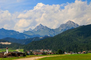 Avusturya 'nın Heiterwang köyüne giden bir yola bakın. Kümülüs bulutlarıyla dolu bir yaz günü.