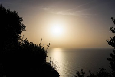 Güneş, Agios Spiridon yakınlarındaki Agios Spiridon adasında sahil siluetine karşı altın renginde batıyor.