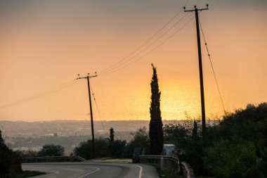 Gün batımında elektrik hatları olan viraj yolu Kıbrıs 20.11.2024