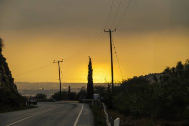 Gün batımında elektrik hatları olan viraj yolu Kıbrıs 20.11.2024