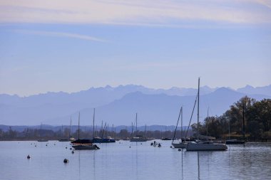 Arka planda tekneler ve dağlar olan göl manzarası.