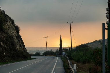 Gün batımında elektrik hatları olan viraj yolu Kıbrıs 20.11.2024