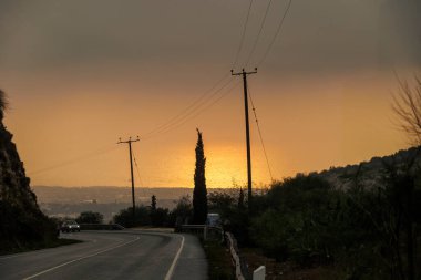 Gün batımında elektrik hatları olan viraj yolu Kıbrıs 20.11.2024