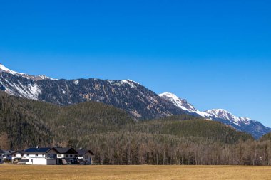 Karlı dağlık yamaçlar, açık bahar gökyüzü altındaki yerleşim evleri, Otztal, Avusturya