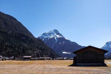 Karlı dağlık yamaçlar, açık bahar gökyüzü altındaki yerleşim evleri, Otztal, Avusturya