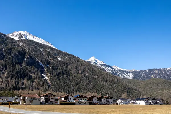 Karlı dağlık yamaçlar, açık bahar gökyüzü altındaki yerleşim evleri, Otztal, Avusturya