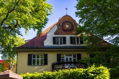 Gable 'da boyalı astronomik saati olan tarihi villa, bahar yapraklarıyla çevrili, Almanya, Augsburg, 30 Nisan 2025