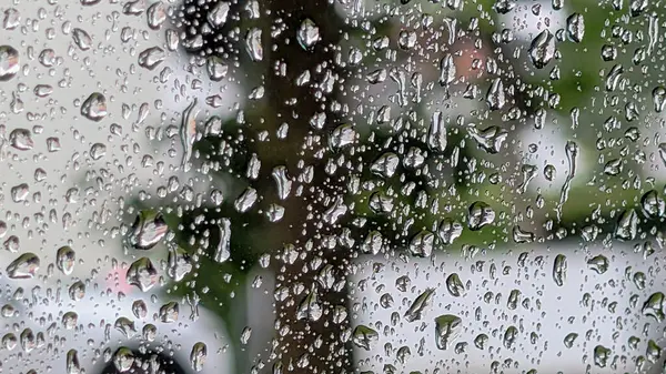 Bulanık yeşil arkaplanlı pencere camında yağmur damlaları