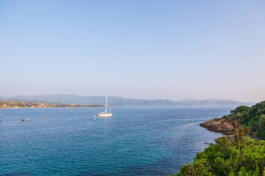 Korsika 'ya demir atmış tekneler ve tepelerle kıyı manzarası.