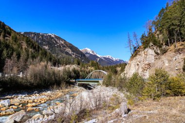 Mavi gökyüzünün altındaki ağaçlarla çevrili dağ nehrinin güzel bir görüntüsü.