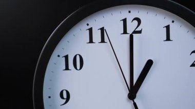 Yuvarlak analog duvar saati, kapalı bir sokette, siyah bir arka planda, soket ise 11 'den 1' e ikinci eli takip eder.