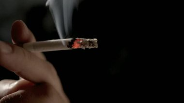Siyah arka planda sönmüş dumanla el ele tutuşmuş sigara.