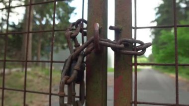 Paslı metal bir çiti kapatan kalın bir zincir. Etrafı ağaçlarla çevrili eski bir sanayi deposu olan bir araziyi koruyor. Güneşli bir günde, atış yavaşça çitlerden uzaklaşıyor..