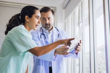 Ortopedik cerrah hastanın diz eklemlerinin röntgenini inceler ve hastalara semptomlar önerir.