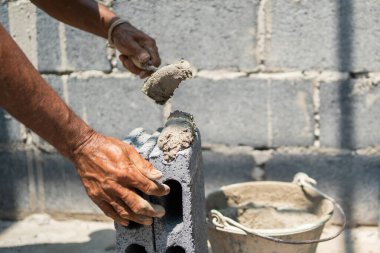 Adam çimento kovasıyla duvar örüyor. Kovanın yarısı dolu ve beton duvarın içine dökülüyor. Adam çimentoyu eşit dağıtmak için mala kullanıyor.