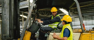 Sarı yelekli iki adam forklift taksisindeler. Biri gülümsüyor.