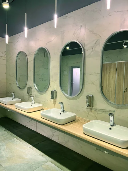 Modern restroom interior with stone gray tiles. Contemporary interior of public toilet. minimal interior with white tiles, round mirrors. Perspective of mens restroom. commercial bathroom.