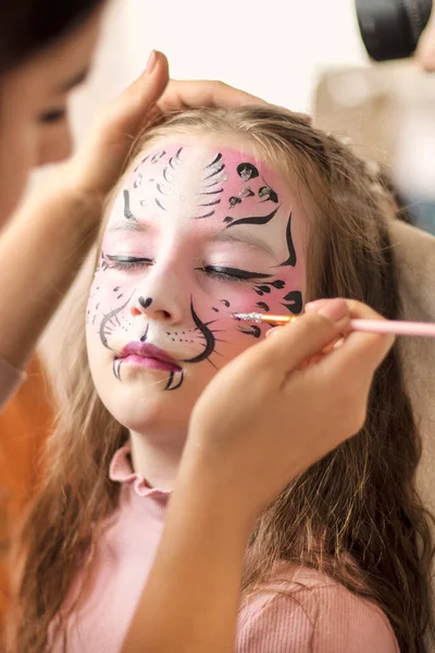 Cute makeup little tiger. face painting outdoors, having fun, copy space. girl with aqua makeup of tiger muzzle. Master making aqua makeup on girl face. aqua grimm on birthday or halloween party
