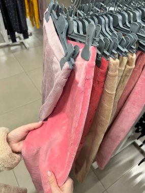 Mağazadaki askılarda renkli pantolonları tutan eller. Pantolon dükkanda. Kadın elbise mağazasından yeni pantolon seçiyor. Eller tezgahtaki kadife pantolona dokunur. Alışveriş. giyim satış kavramı