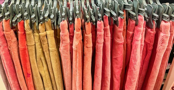 colorful trousers with hanger on rack, cloths shop in shopping mall , colorful fabric, fashion clothes background. pink shades. Row Colorful womens pants hanging on hangers for sale at fashion store