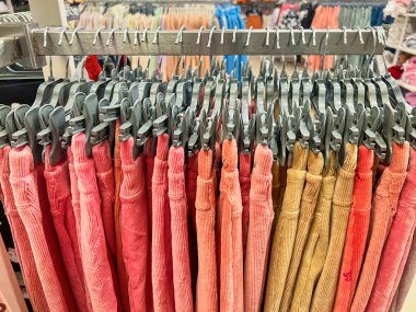 Askıda asılı renkli pantolonlar, alış veriş merkezinde kumaş alışverişi, renkli kumaş, moda kıyafetleri. Pembe gözlükler. Moda mağazasında askılarda asılı renkli kadın pantolonu.