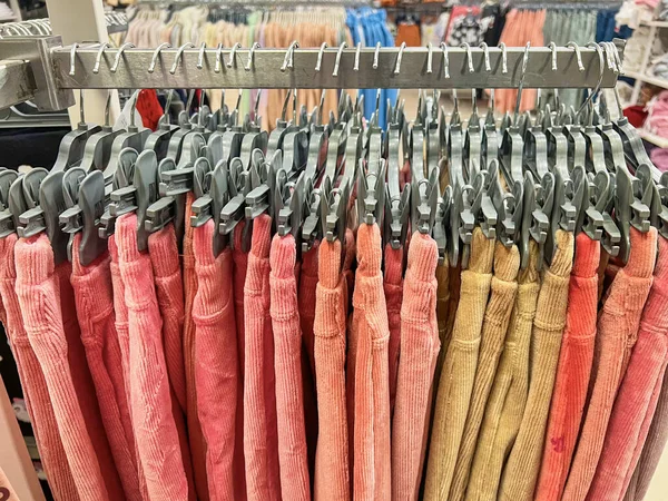 colorful trousers with hanger on rack, cloths shop in shopping mall , colorful fabric, fashion clothes background. pink shades. Row Colorful womens pants hanging on hangers for sale at fashion store