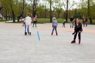 Ukrayna. Kyiv. 23.04.2023 çocuk, dışarıda arkadaşlarıyla paten oynayan gençler. Bir sürü çocuk, çocuklar paten kaymaya gider, yetişkin bir eğitmenle paten kaymayı öğrenir, gölgede mola verir.