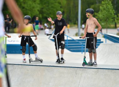 06.03.2022. Ukrayna, Kyiv, VDNG parkı. Koruyucu kasklı çocuklar ve gençler spor sahasında kaykay ve scooterlara biniyorlar. Yüksek kalite fotoğraf