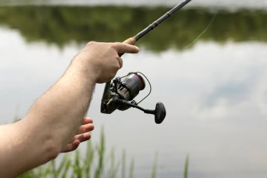 Nehirde dönen balıkçı, elinde oltayı tutuyor ve makarayı çeviriyor, geçmişi bulanık. Erkek eller bir nehrin arka planında dönen bir çubuk tutar.