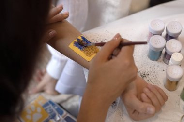 Seçici odaklanma. Çocuklar ve yetişkinler için dekoratif kozmetik. Kutsal Flash dövmesi. Çocuklar için dövme nakli. Usta bir kıza pullu temyporar simli dövme yaptırır. childreay. Canlandırıcılar